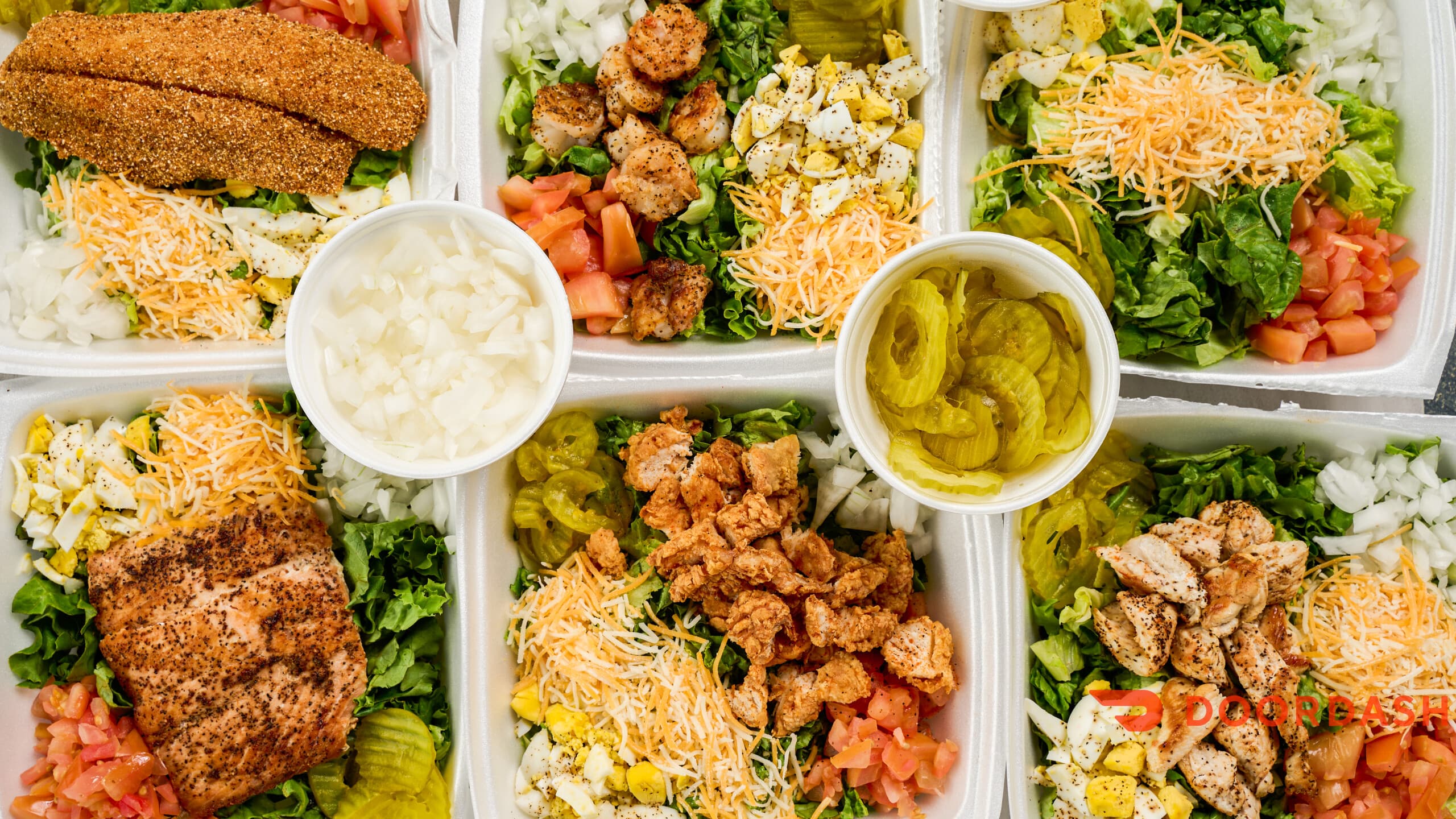 Assorted takeout salads featuring grilled salmon, shrimp, chicken, and fried fish with fresh toppings.